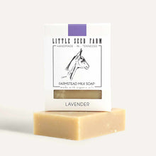 A cream-colored bar of lavender milk soap rests beneath a white Little Seed Farm package with a purple stripe and goat illustration.
