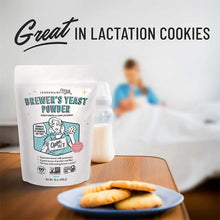 White pouch of Legendairy Milk Brewer's Yeast Powder next to a glass of milk and plate of cookies on a wooden table.