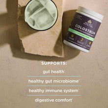 Ancient Nutrition Colostrum powder in Coconut Lime flavor with a glass of mixed powder displayed overhead on a neutral surfac