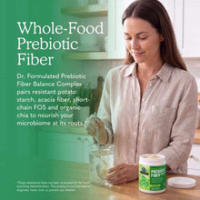 A woman in a linen shirt stirs powder into a glass of water beside an open tub of prebiotic fiber.