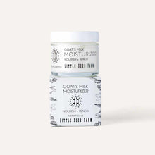 A glass jar of goat's milk moisturizer with a white lid rests on its white box decorated with botanical illustrations.