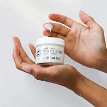 Two hands hold a small jar of Little Seed Farm goat's milk moisturizer while a fingertip lifts a dollop of white cream.
