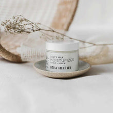 A small jar of Little Seed Farm goat's milk moisturizer with a white lid rests on a speckled ceramic dish beside dried flowers.
