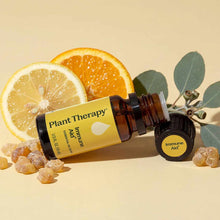 An amber bottle with a yellow Plant Therapy Immune Aid label lies beside lemon and orange slices, eucalyptus leaves, and resin pieces.