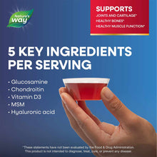 Hand holding small cup of red liquid glucosamine supplement against blue background with ingredient list.