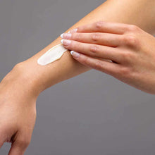 Hand applying white cream to arm against gray background.