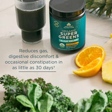 Teal container of Organic SuperGreens + Bloat Relief powder with glass of green beverage, orange slices, and fresh kale.