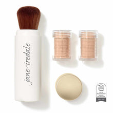 White cylindrical brush applicator with brown bristles, two glass jars of tan powder, one open container of beige powder, and