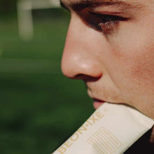 Person in profile holding a BEONIXE product packet with green background.