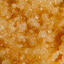 Close-up texture of a golden amber sugar scrub with glossy, coarse crystals clustered together in a thick, oily base.