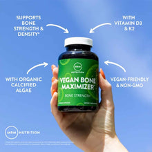 Hand holding dark blue bottle with green label reading "Vegan Bone Maximizer" by MRM Nutrition against blue background with f