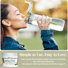 White container of Vitality C Vitamin C Powder with scoop next to woman drinking from water bottle outdoors.
