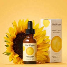 Mad Hippie Vitamin C Serum in amber glass bottle with black dropper, displayed with sunflower and product box on yellow backg