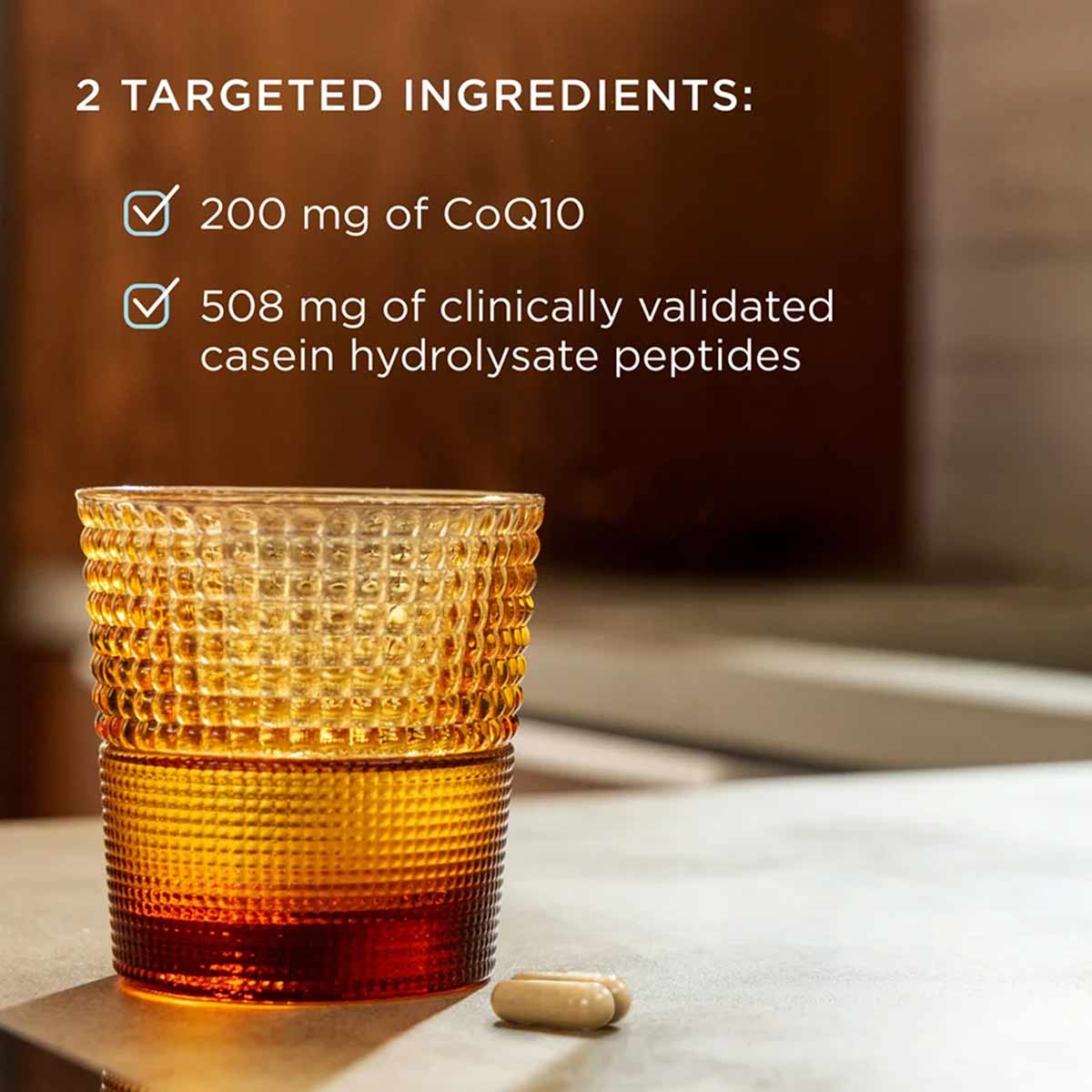 Glass containing amber liquid with text listing 200 mg CoQ10 and 508 mg casein hydrolysate peptides, with capsule beside it.