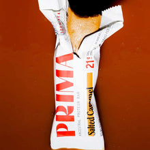 PRIMA Ancestral Protein Bar in Salted Caramel flavor, partially unwrapped to show golden bar interior.