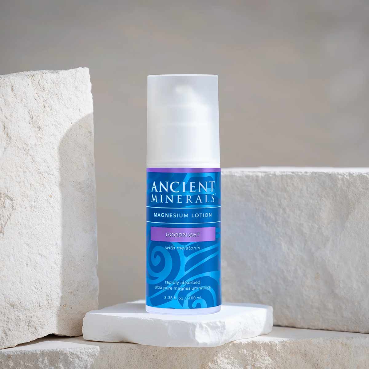 White bottle with blue label reading "Ancient Minerals Magnesium Lotion Goodnight with melatonin" displayed on white stone bl