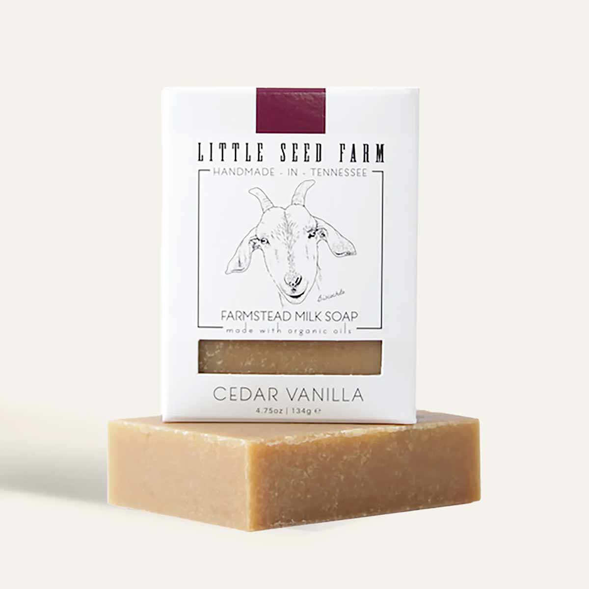 A tan bar of soap rests beneath a white Little Seed Farm box showing a goat illustration and Cedar Vanilla label.