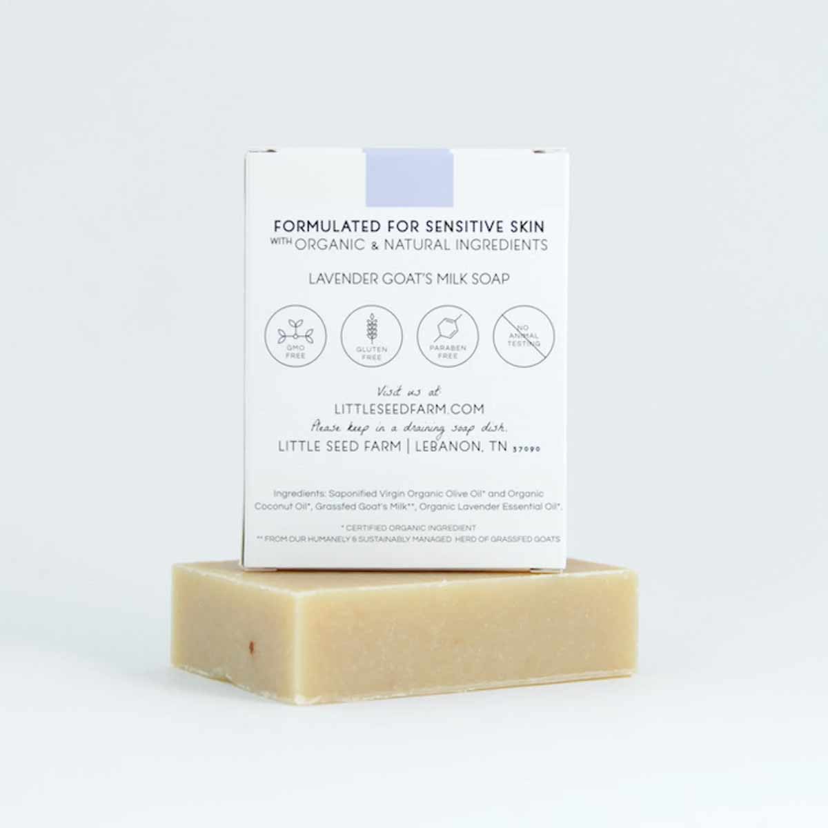 A cream-colored bar of soap rests beneath a white box printed with lavender goat's milk soap details and ingredients.