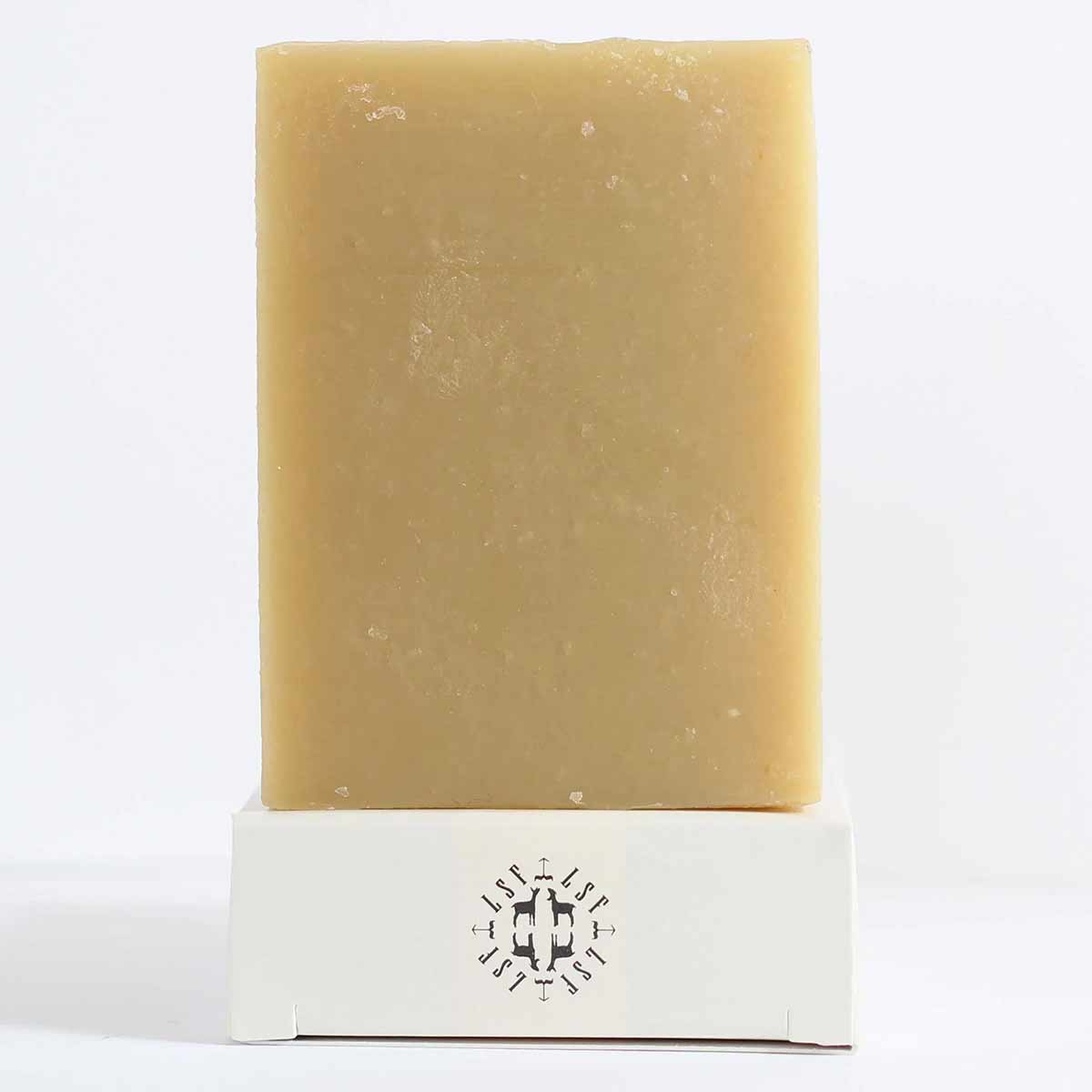 A rectangular tan bar of soap stands upright on a white box printed with a black LSF emblem.