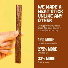 A hand holds a single brown meat stick against a yellow background beside a brown panel with nutrition claims in cream text.