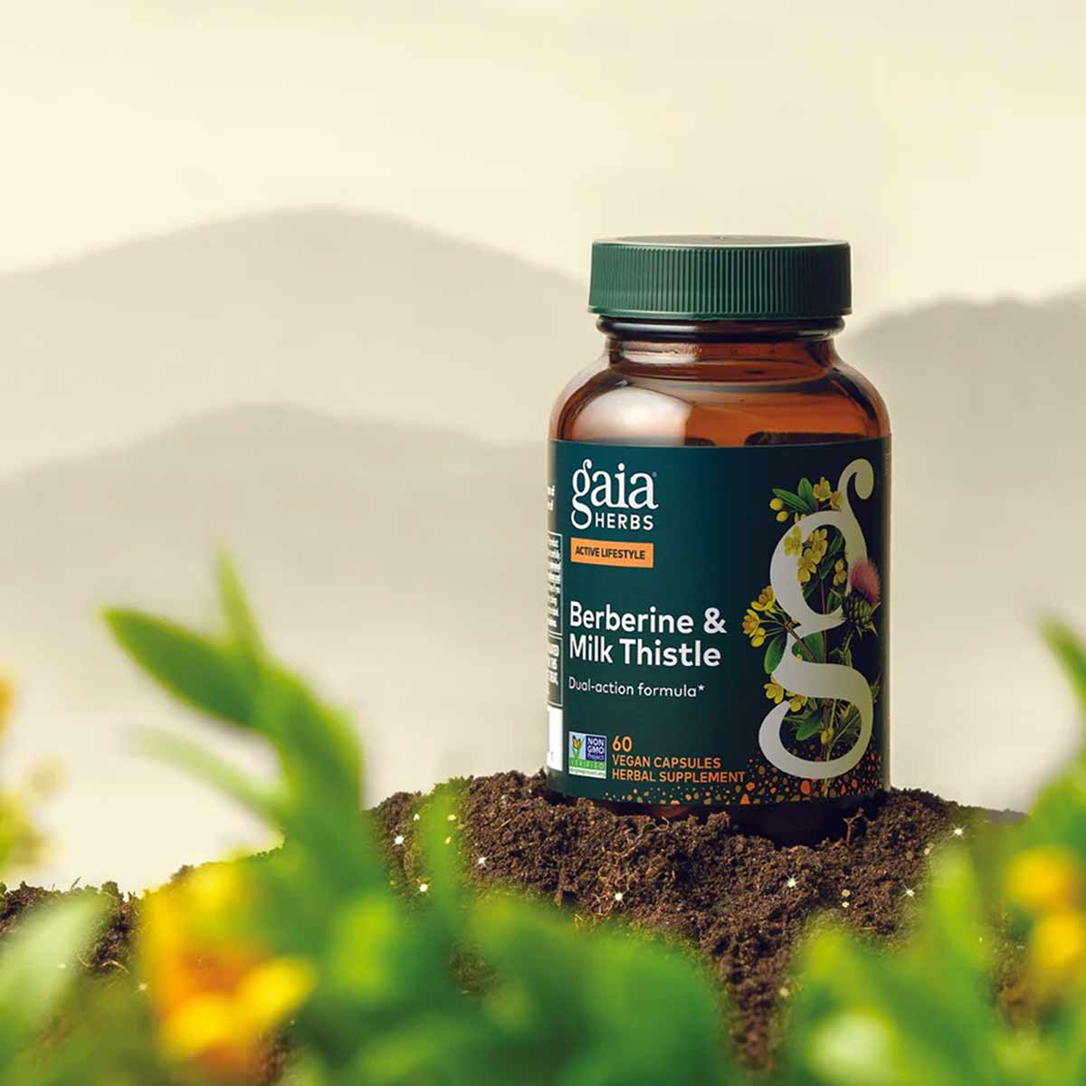Gaia Herbs Berberine & Milk Thistle amber glass bottle with green cap sitting on soil surrounded by green leaves and yellow f