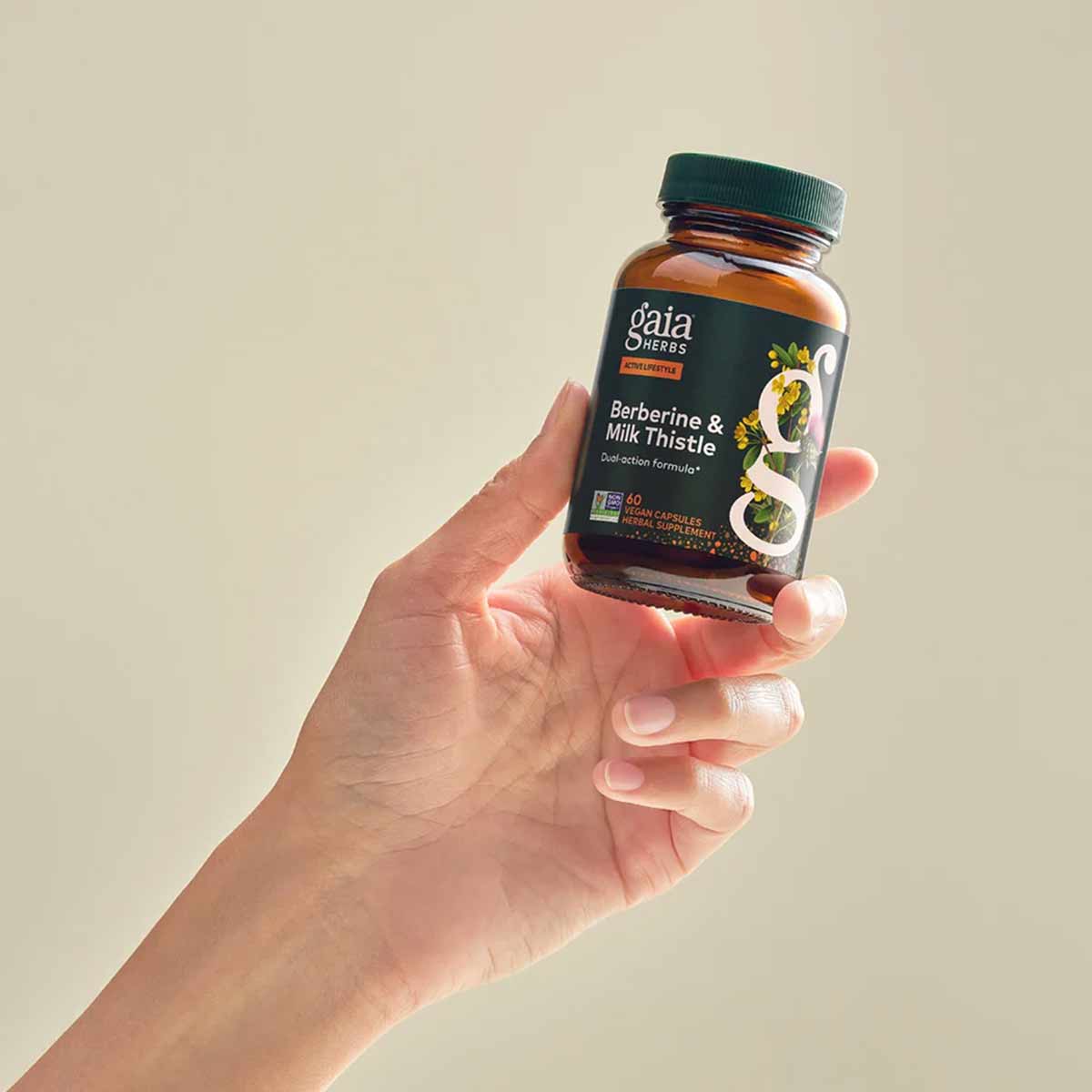 Amber glass bottle of Gaia Herbs Berberine & Milk Thistle supplement held in hand against neutral background.