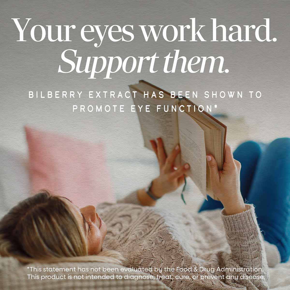 Person reading a book while resting on a couch with pink and blue pillows nearby.