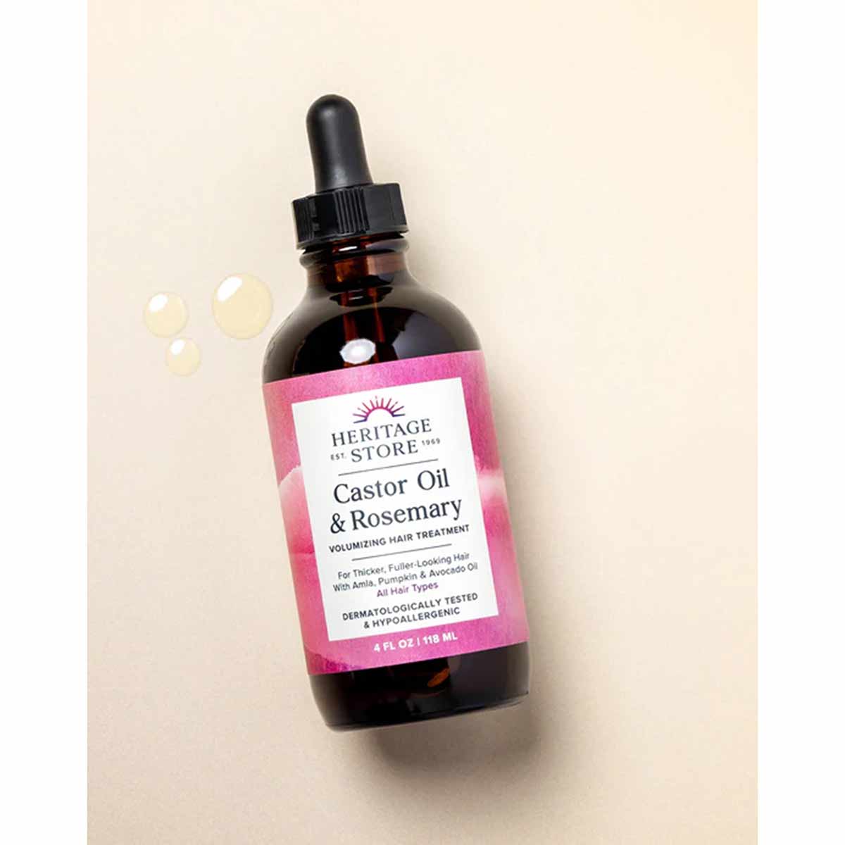 Dark amber glass dropper bottle with pink and white label reading "Heritage Store Castor Oil & Rosemary Volumizing Hair Treat