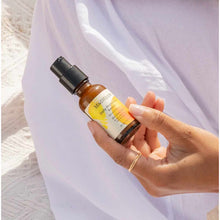 Brown glass bottle with black pump dispenser held in hand against white fabric background.