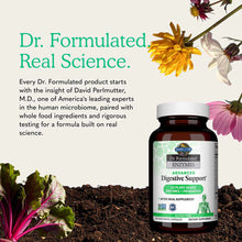 A brown supplement bottle with a white cap and green label sits on soil beside colorful flowers and leafy greens.