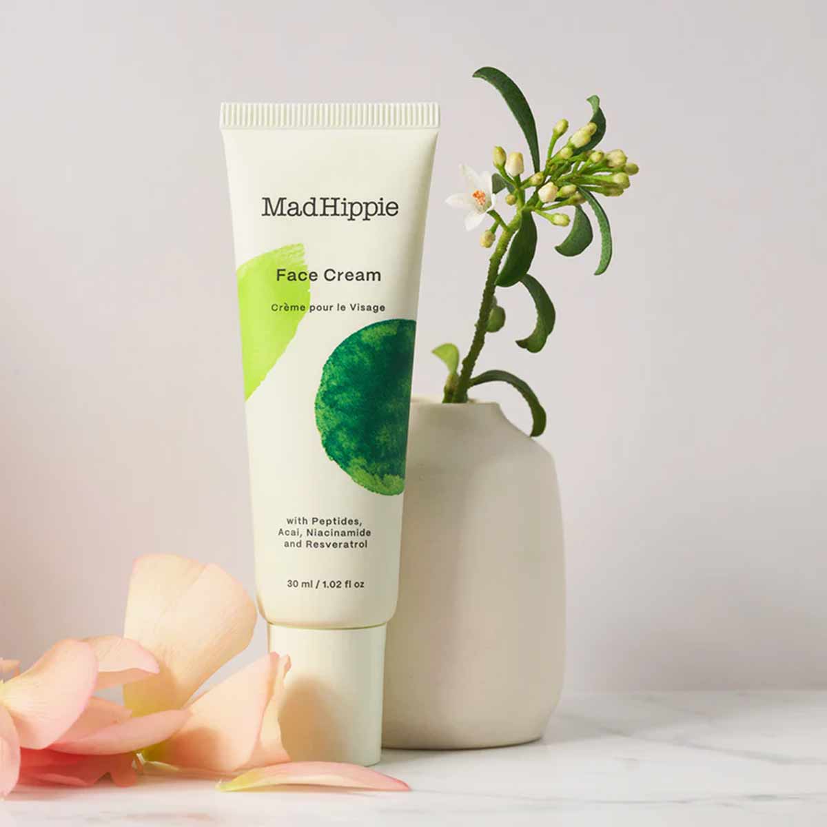 Mad Hippie Face Cream 1.02 oz tube with green and white label, displayed with potted plant and rose petals.