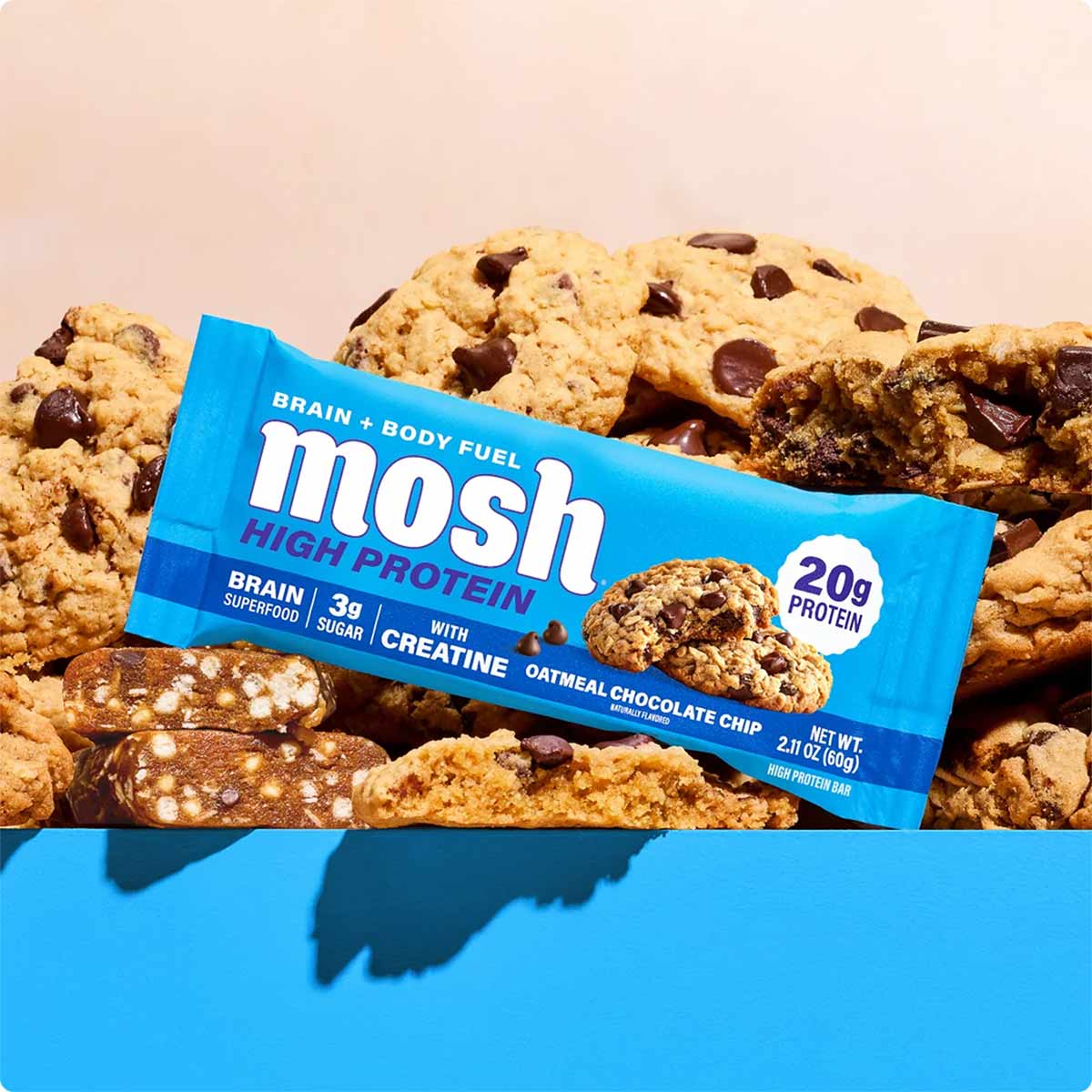 MOSH high protein bar with creatine in blue packaging surrounded by oatmeal chocolate chip cookies.