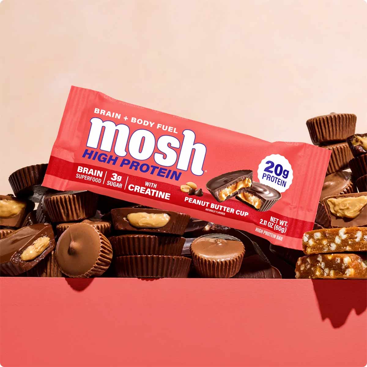 Red MOSH High Protein bar with creatine in peanut butter cup flavor surrounded by chocolate candies.