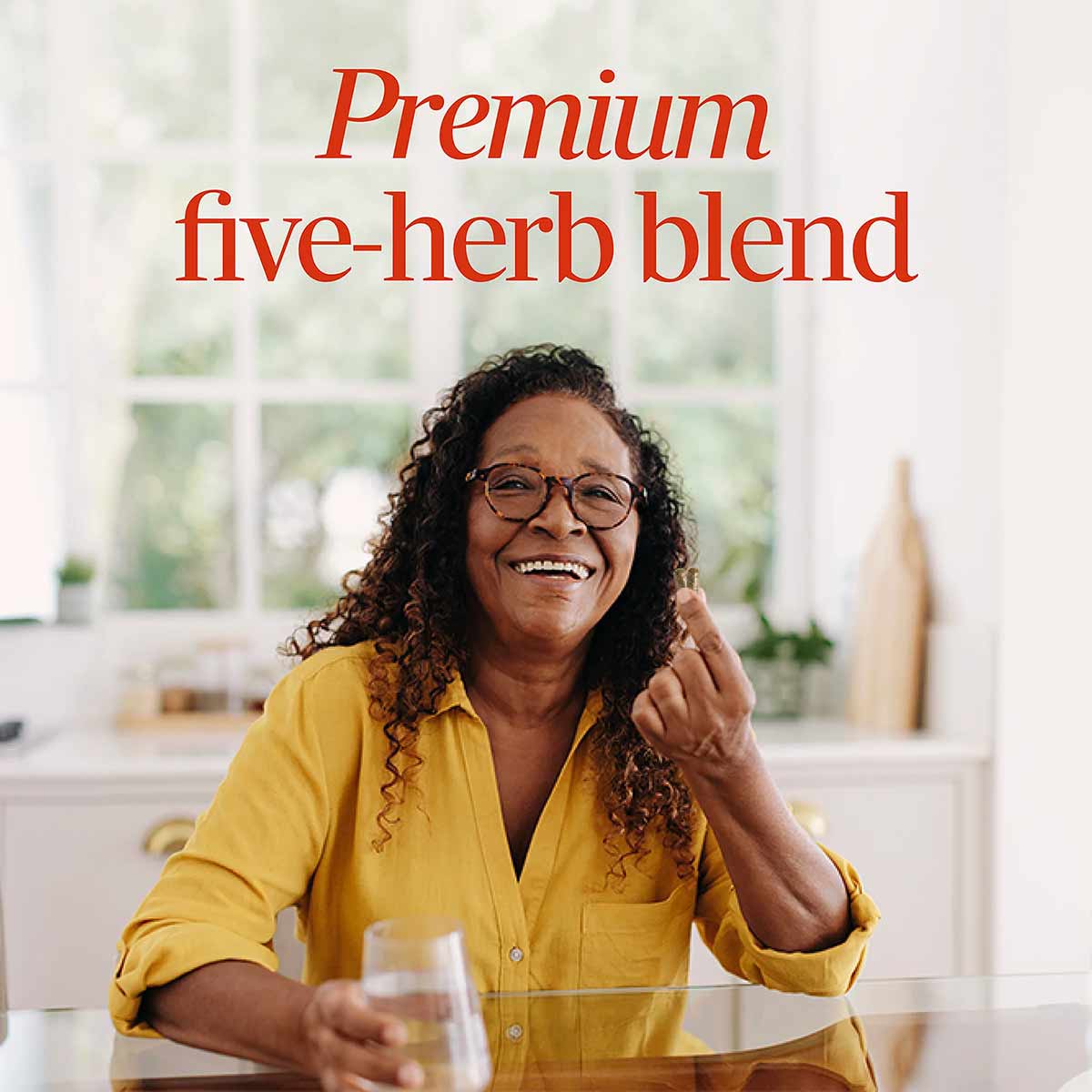 Woman in yellow shirt smiling at table with glass of water and text reading "Premium five-herb blend."