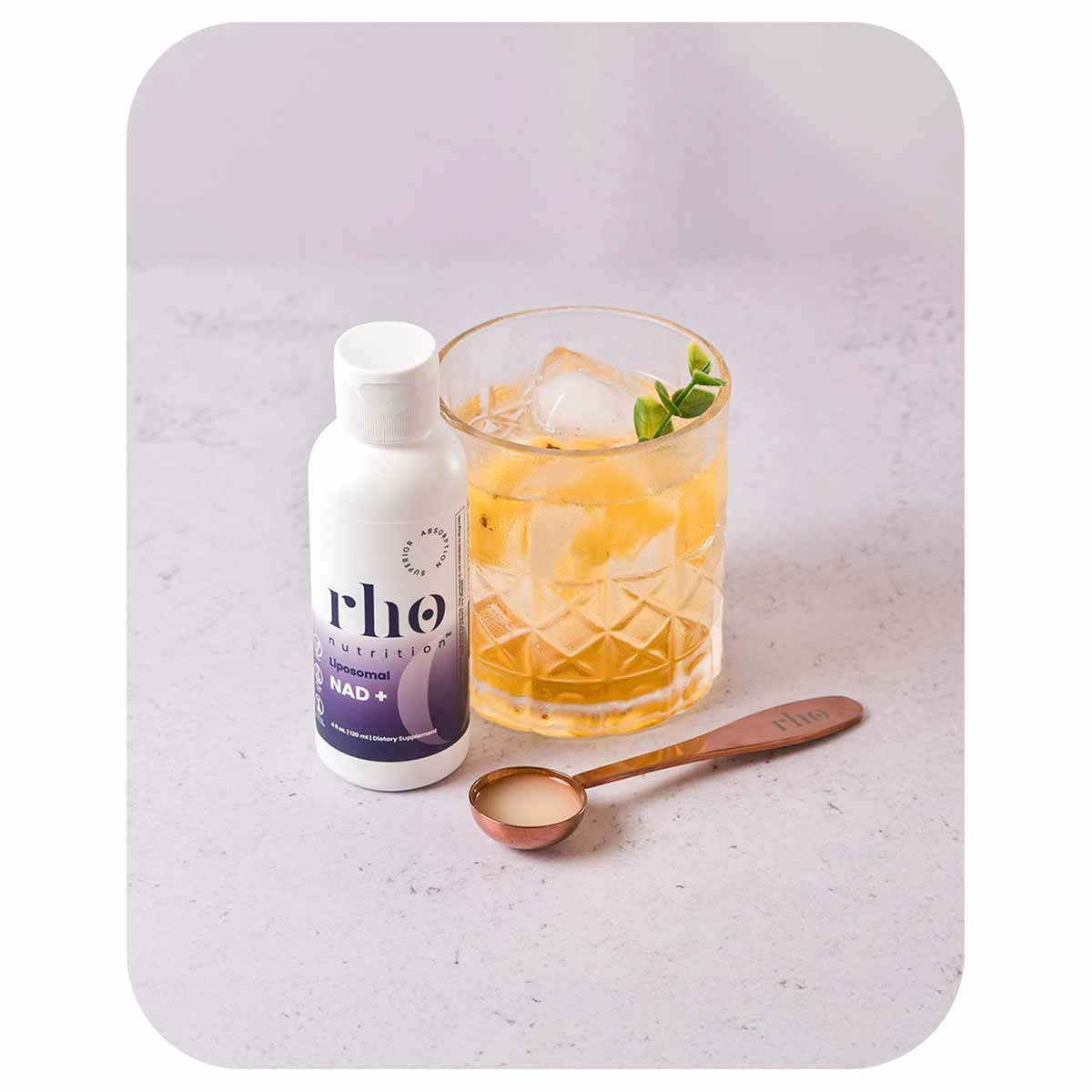 White Rho Nutrition bottle with purple label next to glass of amber liquid, ice, and mint with wooden measuring spoon.