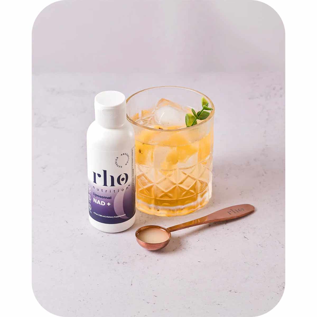 Rho Nutrition liposomal NAD+ bottle displayed with a glass of amber liquid, ice, mint, and a measuring spoon.