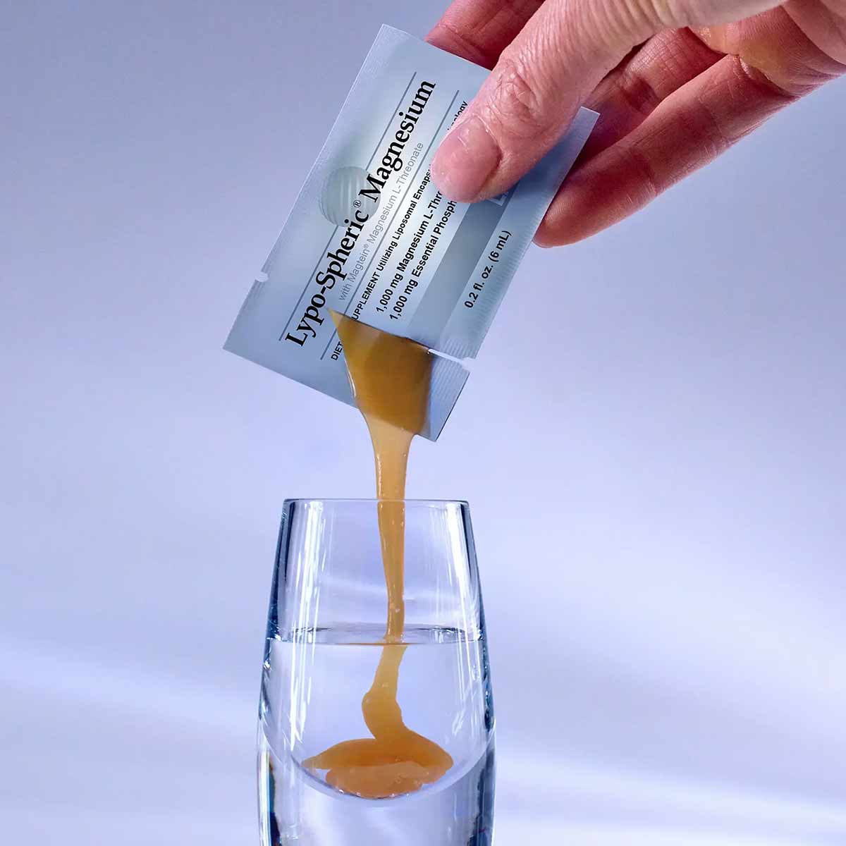 Hand pouring golden liquid from Lypo-Spheric Magnesium packet into clear glass.