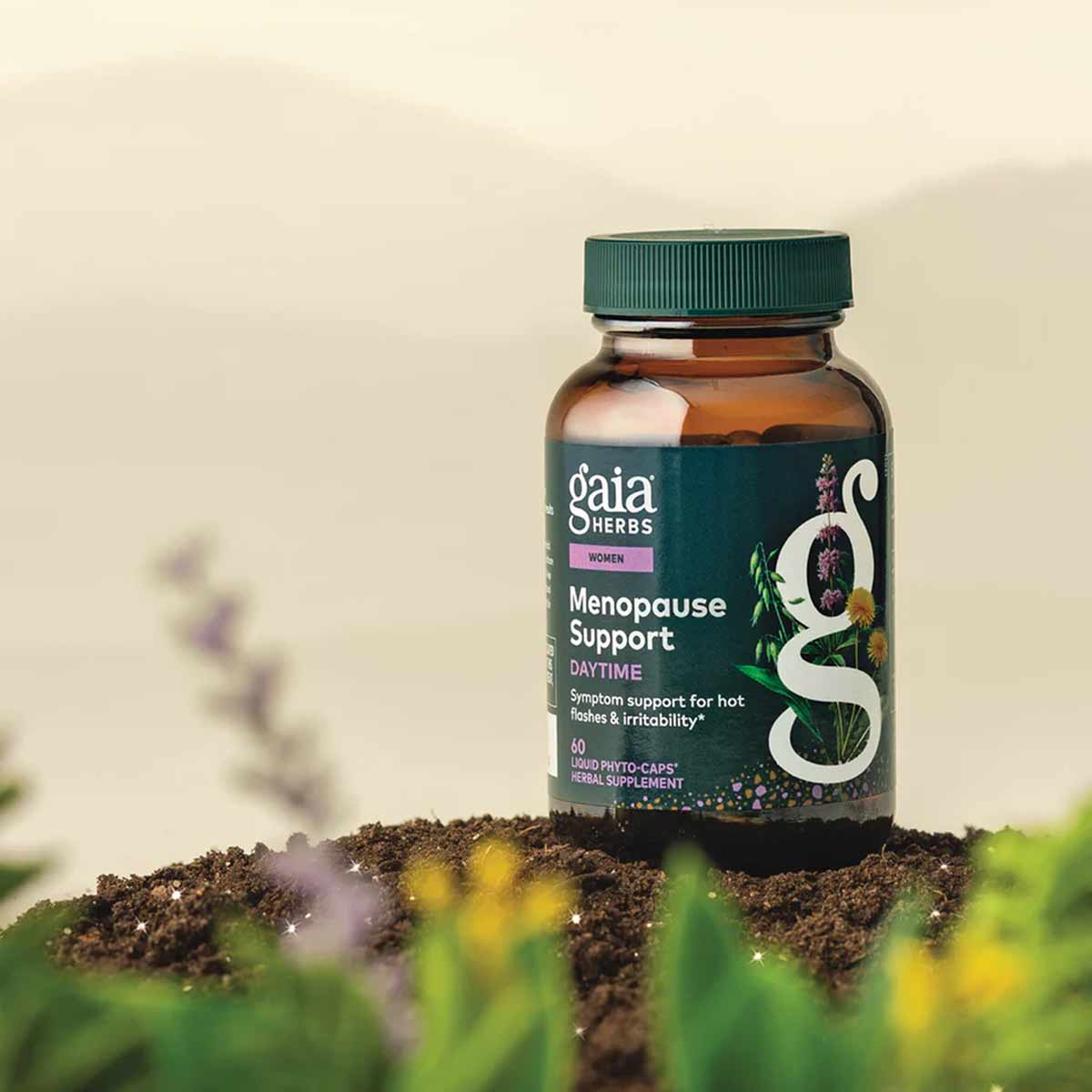 Gaia Herbs Menopause Support Daytime supplement bottle with green cap and dark teal label on soil with plants.