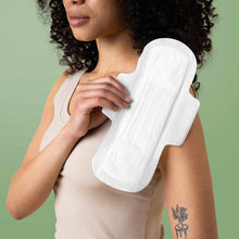 A woman with curly dark hair in a beige tank top holds a large white pad with wings against her shoulder.