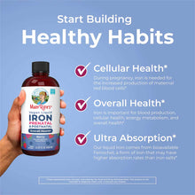 Hand holding a dark amber glass bottle of MaryRuth's vegan liquid iron supplement with berry flavor label against blue backgr