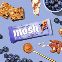 MOSH Blueberry Almond Crunch protein bar with 12g protein surrounded by blueberries, almonds, and apple slices on blue backgr