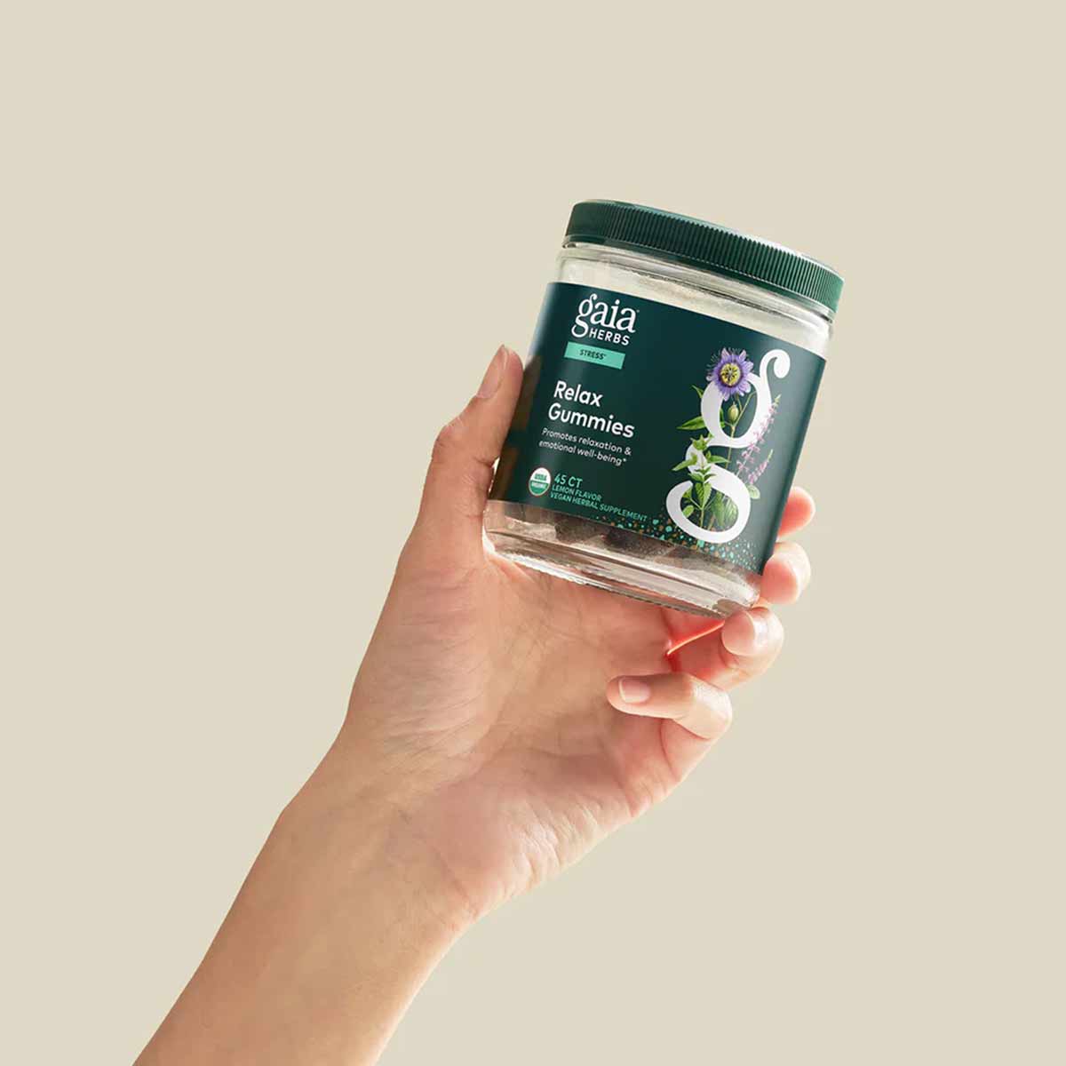 Hand holding Gaia Herbs Relax Gummies bottle with green label and clear container against beige background.
