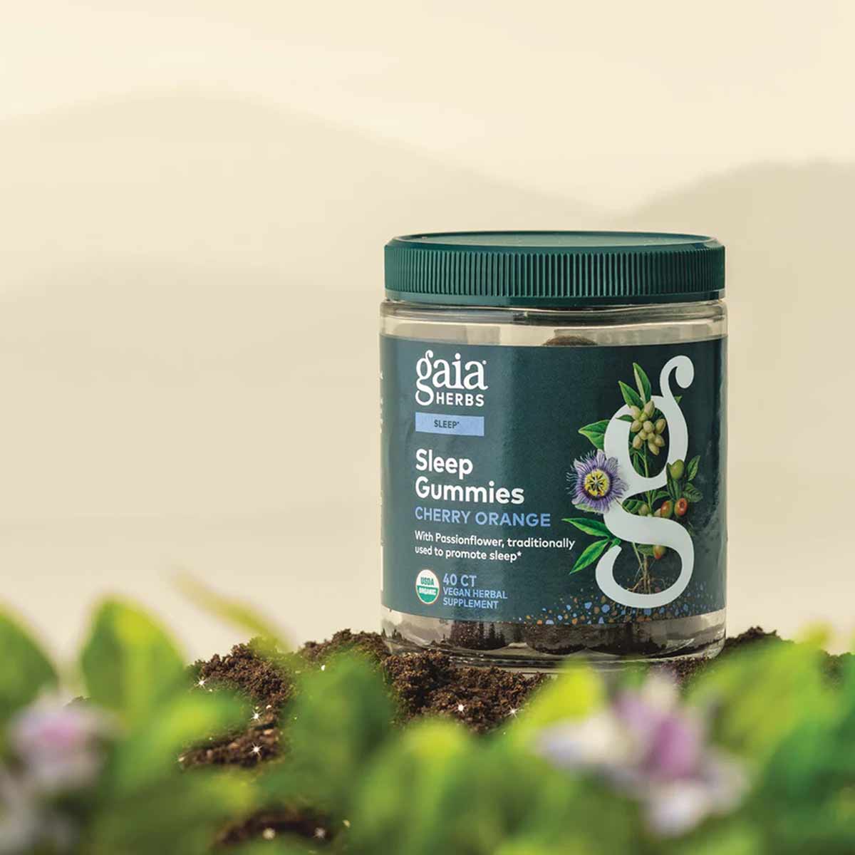 Gaia Herbs Sleep Gummies bottle with teal label and cap, 40 count, displayed on soil with blurred flowers.