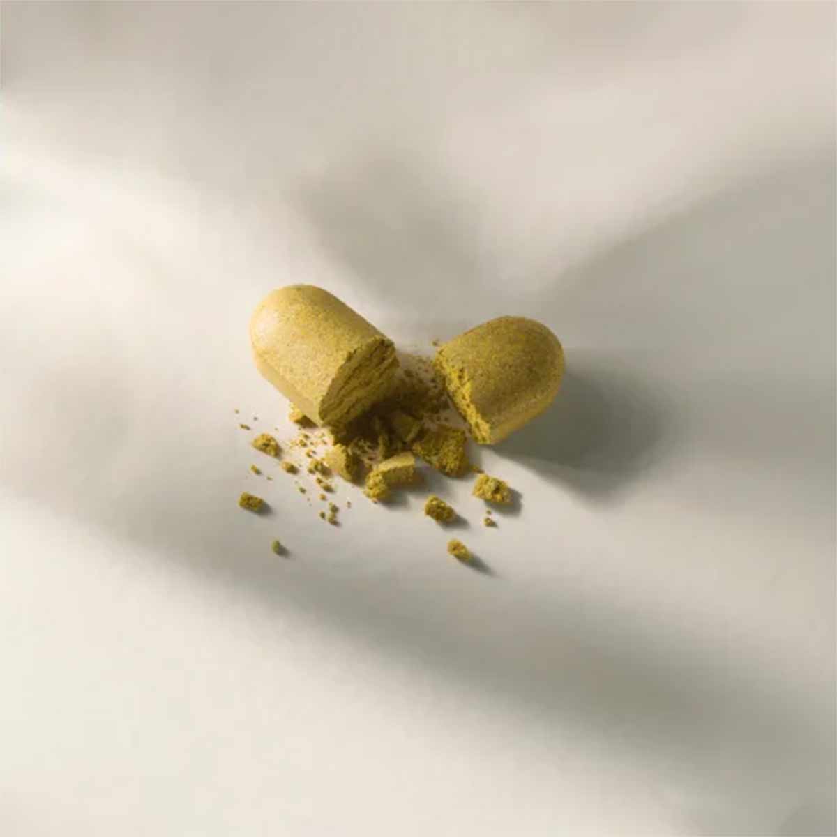 Open capsule containing yellowish-green powder with scattered particles on white surface.