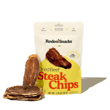 A cream and yellow Rodeo Snacks pouch of dried beef steak chips stands beside a stack of thin beef slices.