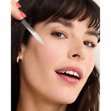 Person applying white serum with dropper applicator to cheek area.