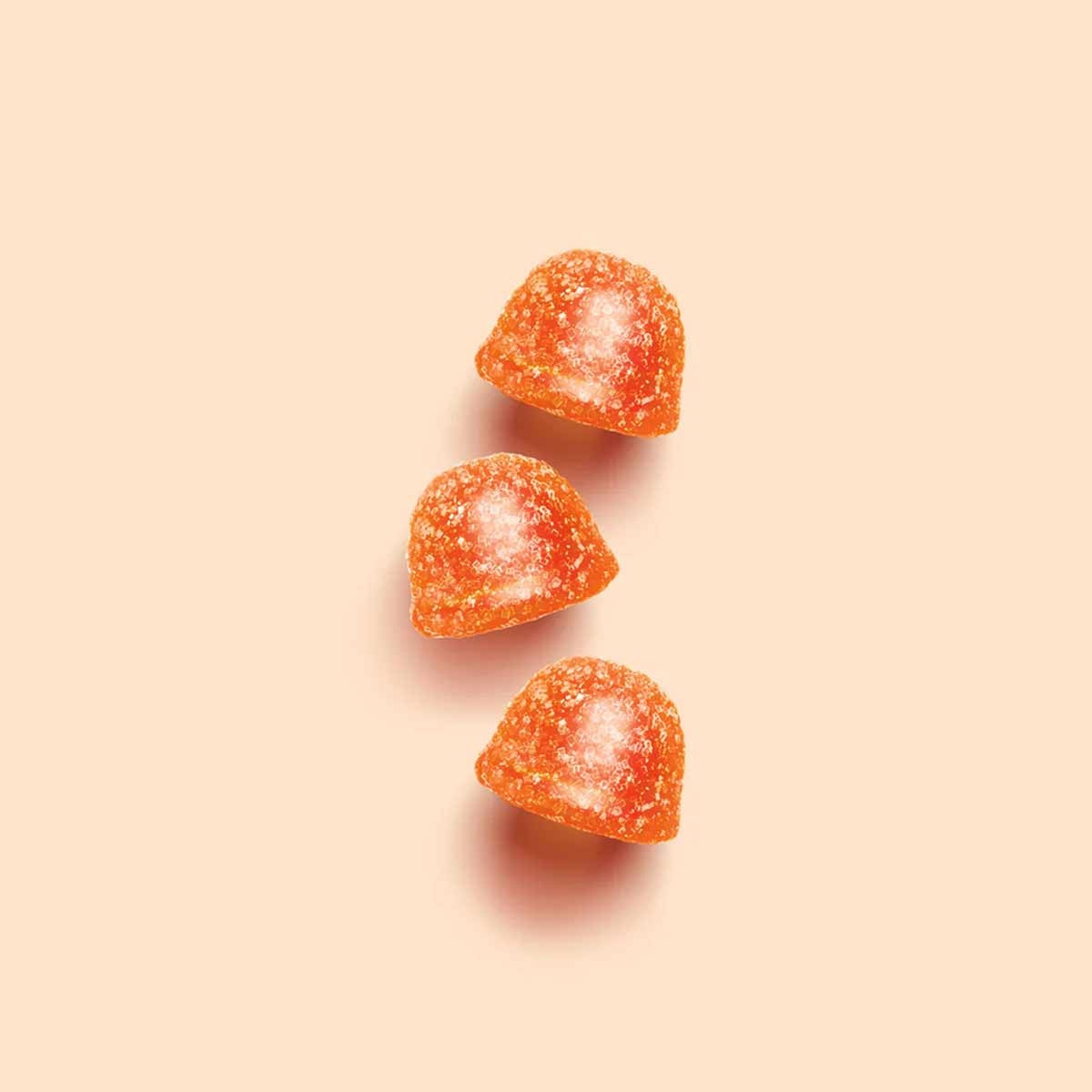 Three orange gummy vitamins coated in sugar on a beige background.