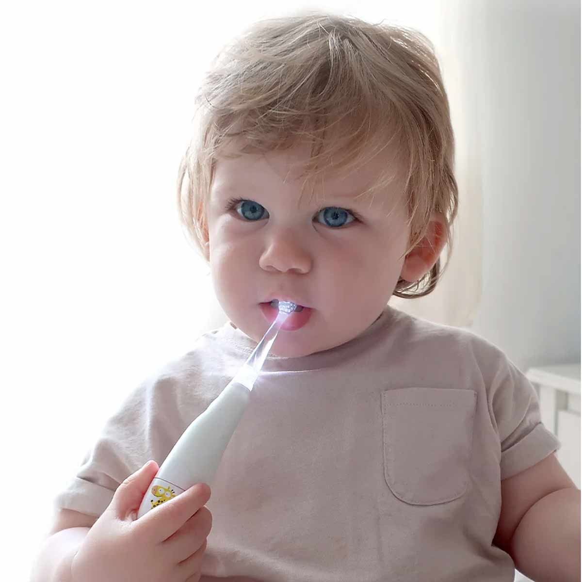 Toddler with light hair holding a white and pink sonic toothbrush with illuminated bristles in mouth.